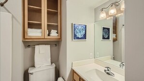 A bathroom with a toilet, a cabinet with towels, a sink with a mirror, and two framed pictures on the wall.