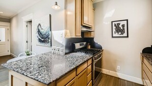 A kitchen with granite countertops, wooden cabinets, a stove, and pendant lighting.