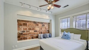 A bedroom with a brick accent wall, a bed with white bedding, and a ceiling fan.