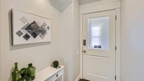 A hallway with a white door marked "808," a framed abstract artwork on the wall, and a small white console table with green bottles and a plant.