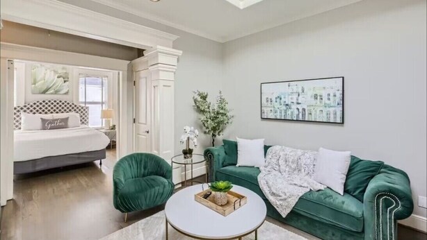 A modern living room with a bed, green armchairs, a coffee table, and artwork on the walls.