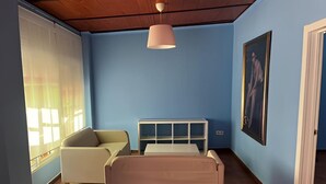 Een slaapkamer met een bed, een stoel, een nachtkastje, een hanglamp en een raam met gordijnen.