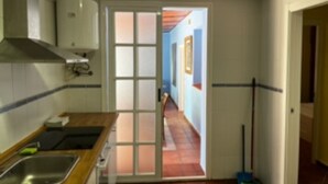 Een smalle keuken met een betegelde spatwand, een houten aanrechtblad en een RVS spoelbak.
