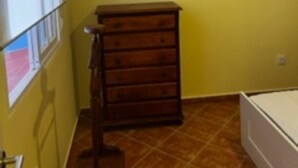 Een kamer met gele muren, een houten dressoir, een bed en een raam met zonwering.