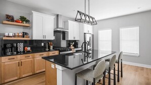 A modern kitchen with a central island, wooden cabinets, and a black countertop. - Modern 3-bedroom home with fenced yard + easy parking (Indianapolis)