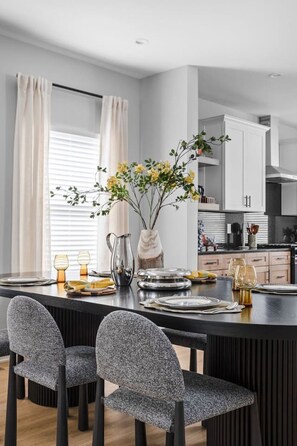 A modern kitchen with white cabinets, a black countertop, and a dining area with a black table and grey chairs.
