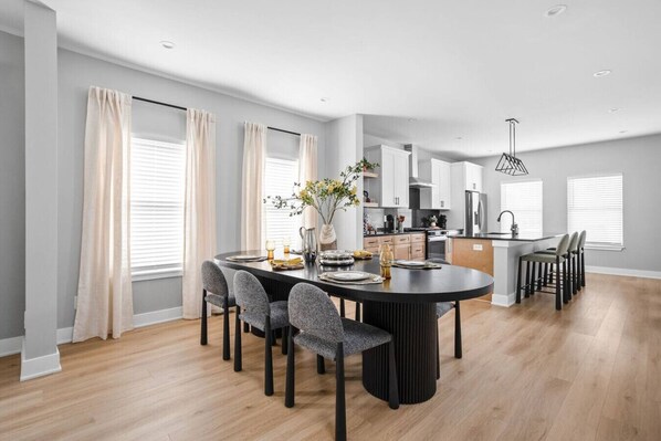 A modern kitchen with white cabinets, a central island, and a dining area with a round table and chairs.