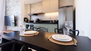 A modern kitchen with a dining area, featuring a flat-screen TV, a stainless steel refrigerator, and a dining table set with plates and cutlery.