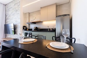 A modern kitchen with a dining area, featuring a flat-screen TV, a stainless steel refrigerator, and a dining table set with plates and cutlery.