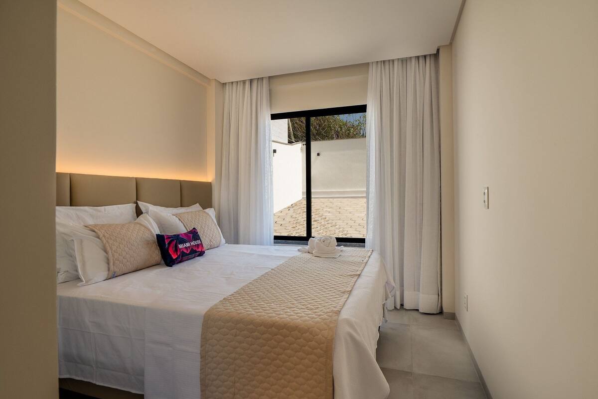 A hotel room with a bed, a headboard, a window with curtains, and a view of the outside.