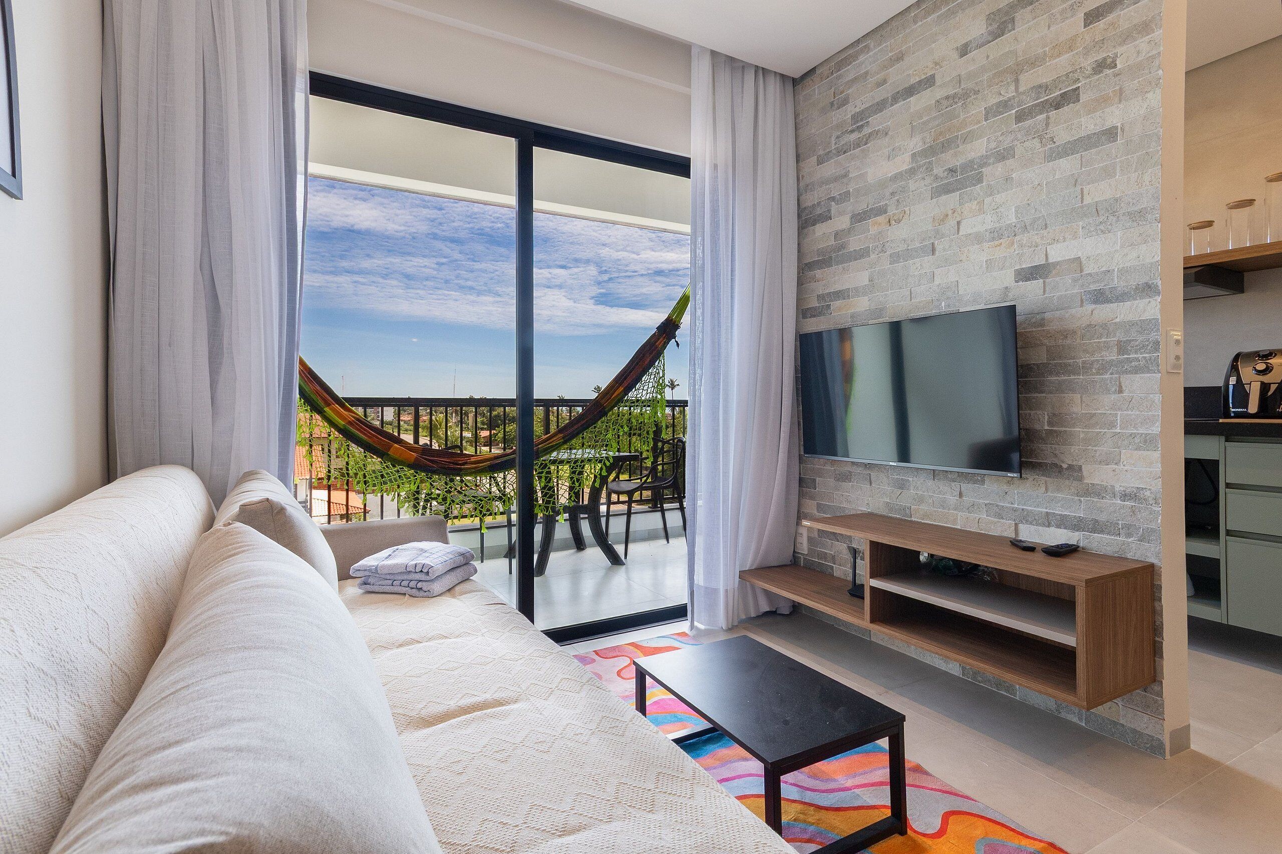 Una sala de estar moderna con sofá, televisión, hamaca y balcón con vistas.