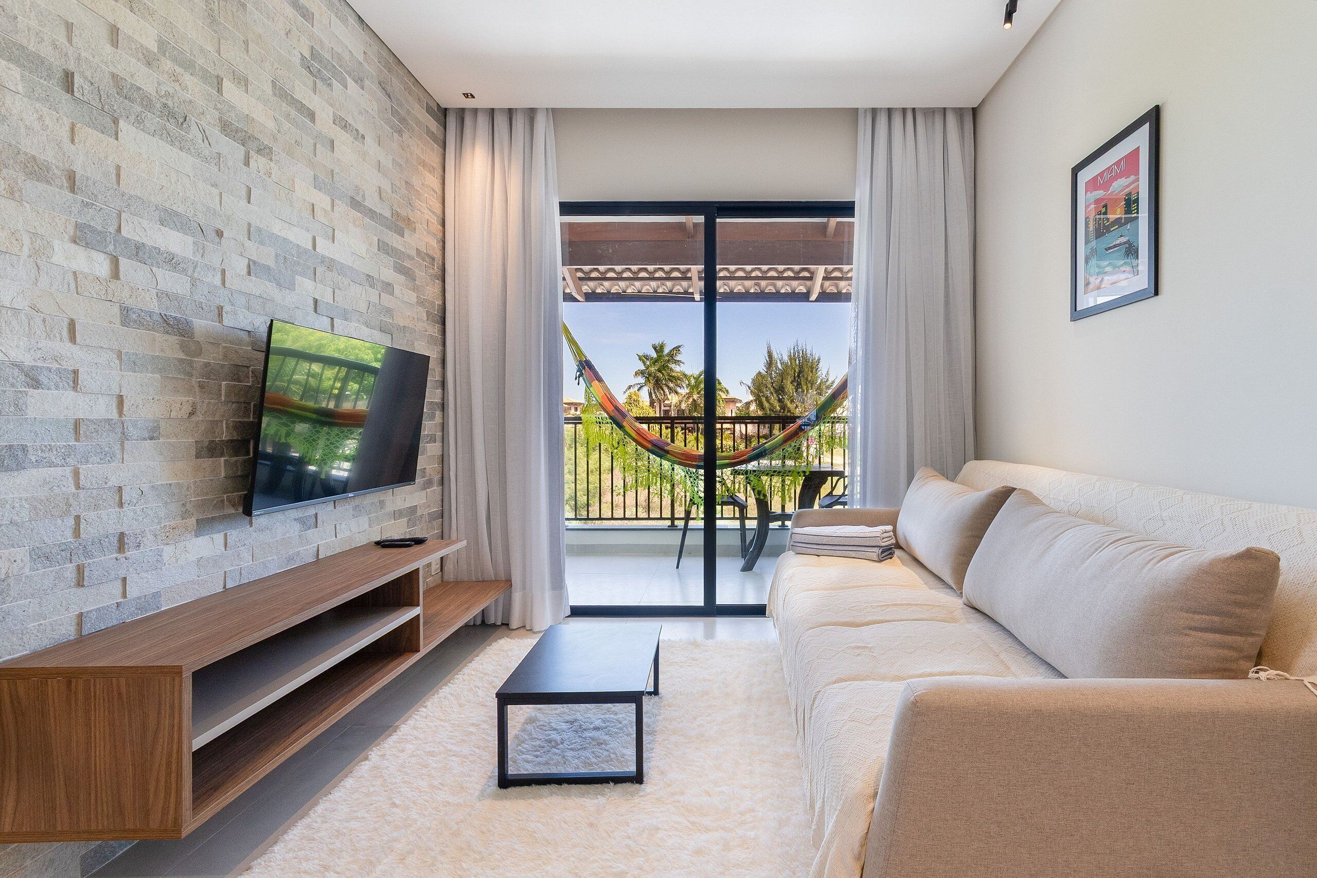 Uma sala de estar moderna com uma TV em uma parede de tijolos, um sofá, uma mesa de centro e uma varanda com uma rede.