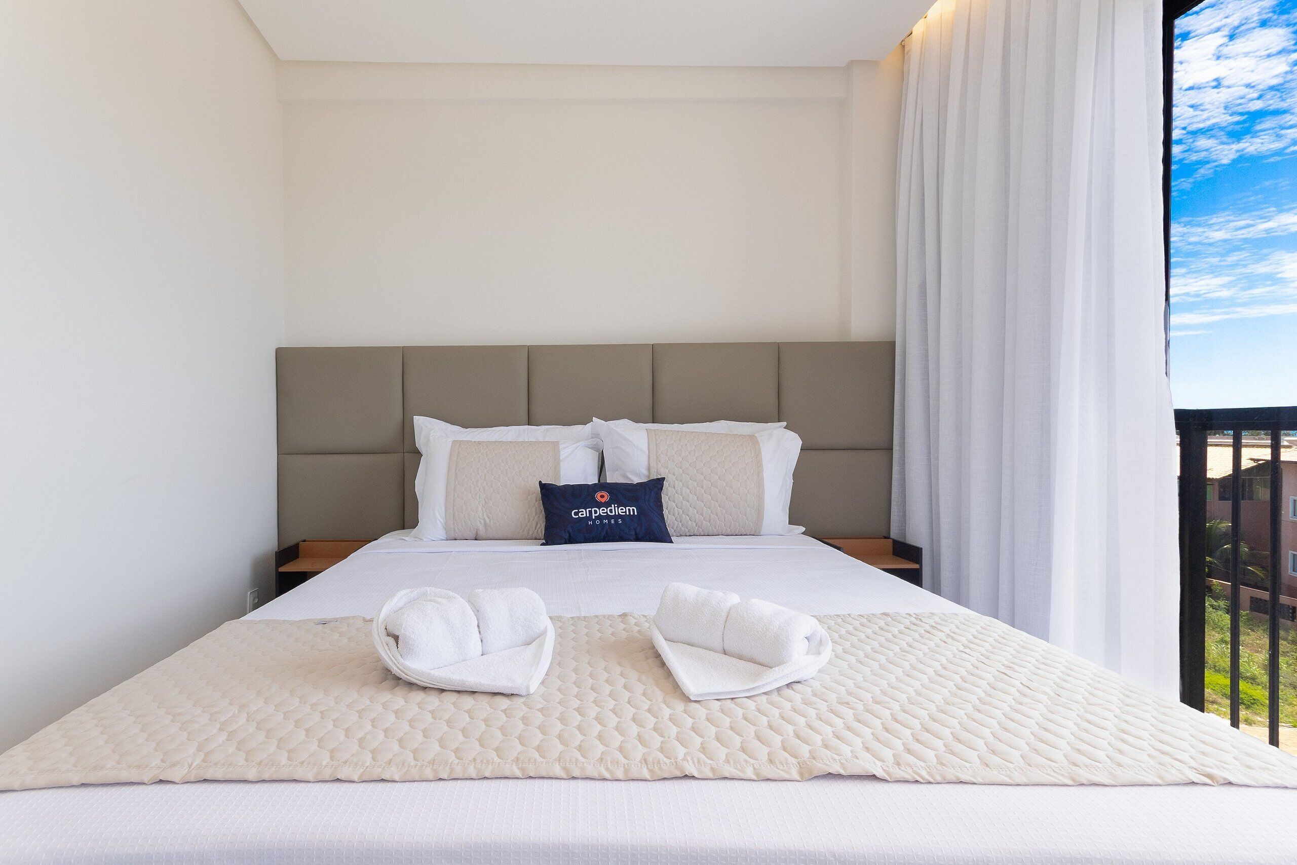 A hotel room with a large bed, a headboard, a pillow with the hotel name, a blanket, and towels on the bed.