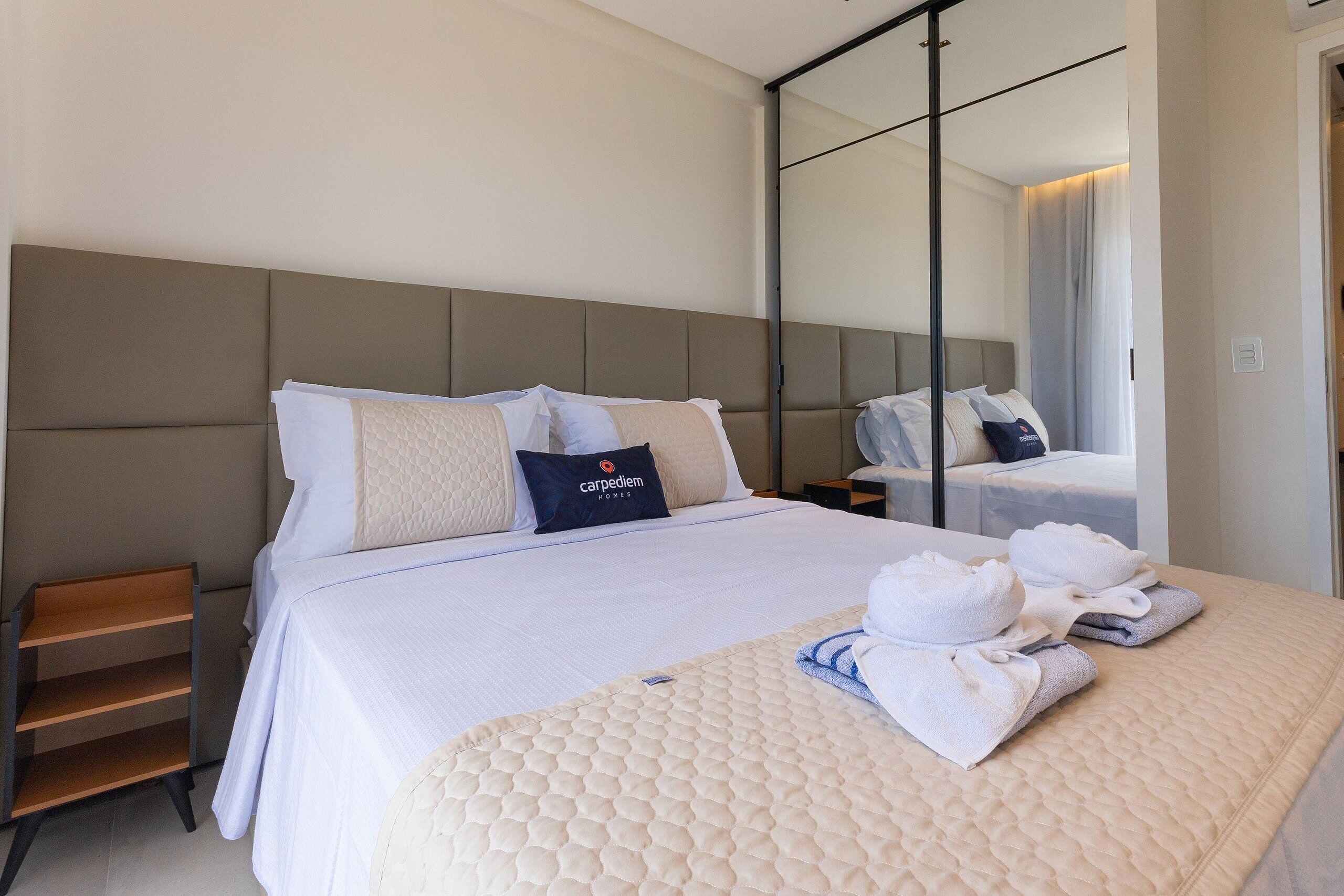 A hotel room with a large bed, a nightstand, a mirror, and neatly folded towels.