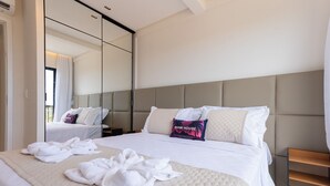 A hotel room with a large bed, a mirror, a bedside table, and a wooden nightstand.