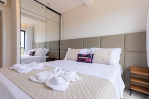 A hotel room with a large bed, a mirror, a bedside table, and a wooden nightstand.