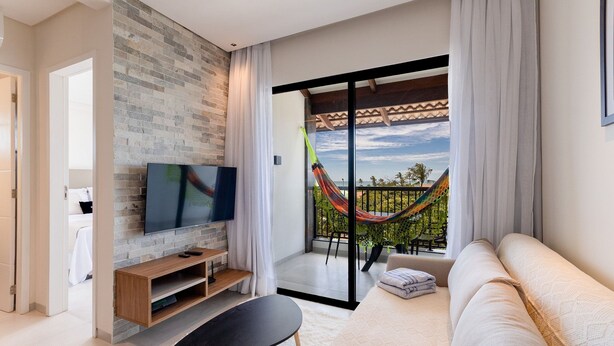 A modern living room with a flat-screen TV, a sofa, a small table, and a balcony with a hammock.