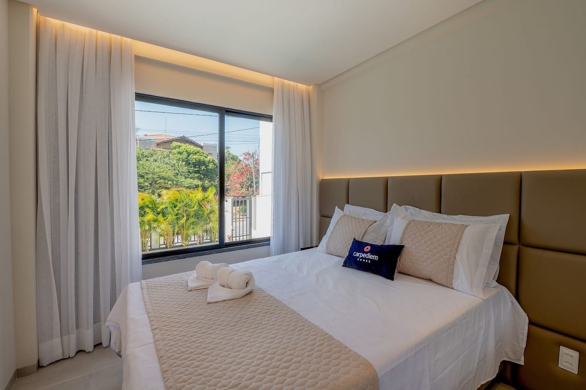 A hotel room with a large bed, a view of greenery outside, and a modern headboard.