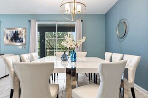 A dining room with a large table, white chairs, a chandelier, and a vase with flowers.