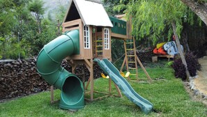 A wooden playhouse with a green slide and climbing wall.