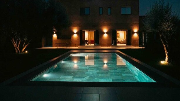 Een modern huis met zwembad, verlicht door buitenverlichting, en zichtbare deur en ramen.