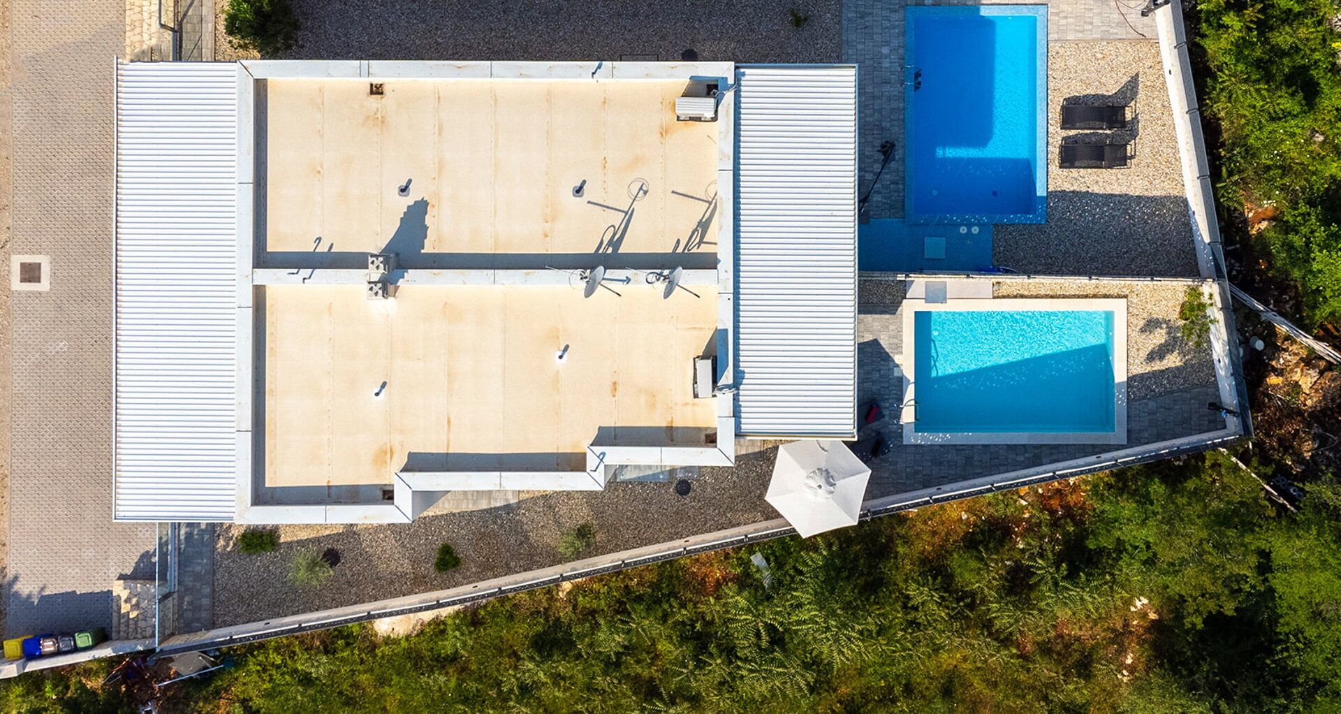 Vista aérea de un edificio con piscina en la azotea, un patio cubierto y un pequeño jardín.