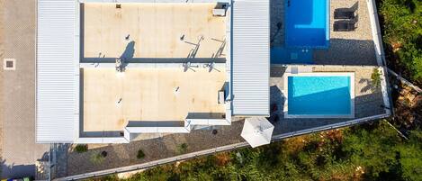 Vista aérea de un edificio con piscina en la azotea, un patio cubierto y un pequeño jardín.