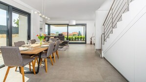 A modern dining area with a wooden table and chairs, a large window with a view of the outdoors, and a staircase with metal railings. - Villa Felice with Pool (Malinska)