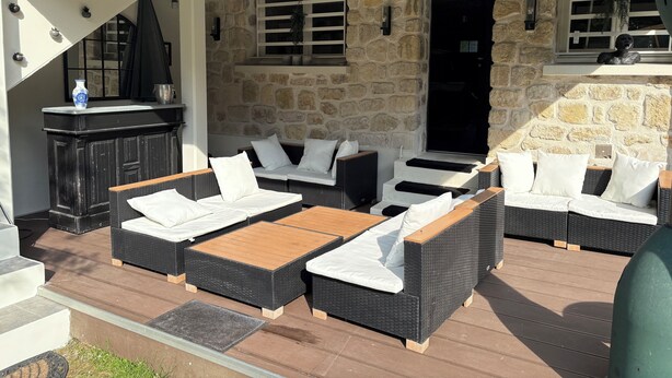 A covered outdoor seating area with wicker furniture and a stone wall backdrop. - A HAVEN OF PEACE ON THE OUTSKIRTS OF PARIS (Clamart)
