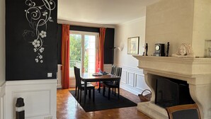 A dining area with a wooden table and chairs, a fireplace, and a view through a glass door. - A HAVEN OF PEACE ON THE OUTSKIRTS OF PARIS (Clamart)
