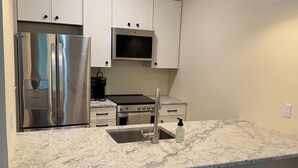 A modern kitchen with white cabinets, stainless steel appliances, a granite countertop, and two bar stools. - Cozy Lakeview Stay by the Beach (Rehoboth Beach)