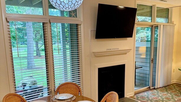A dining area with a round table, wicker chairs, a fireplace, and a TV mounted on the wall. - Cozy Lakeview Stay by the Beach (Rehoboth Beach)