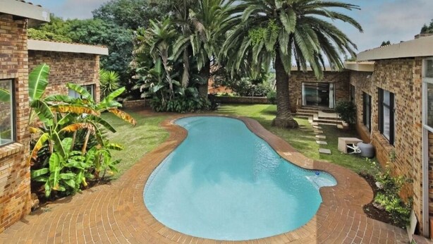 Una piscina rodeada de muros de ladrillo y exuberante vegetación, con palmeras y plantas de banano.
