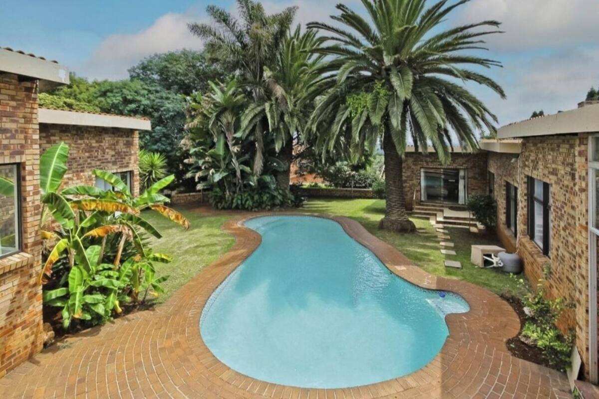 Ein Swimmingpool, umgeben von Backsteinmauern und üppiger Vegetation, darunter Palmen und Bananenpflanzen.