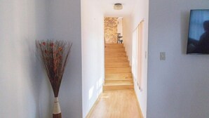 Un pasillo con una escalera de madera que lleva a una habitación con pared de ladrillo.