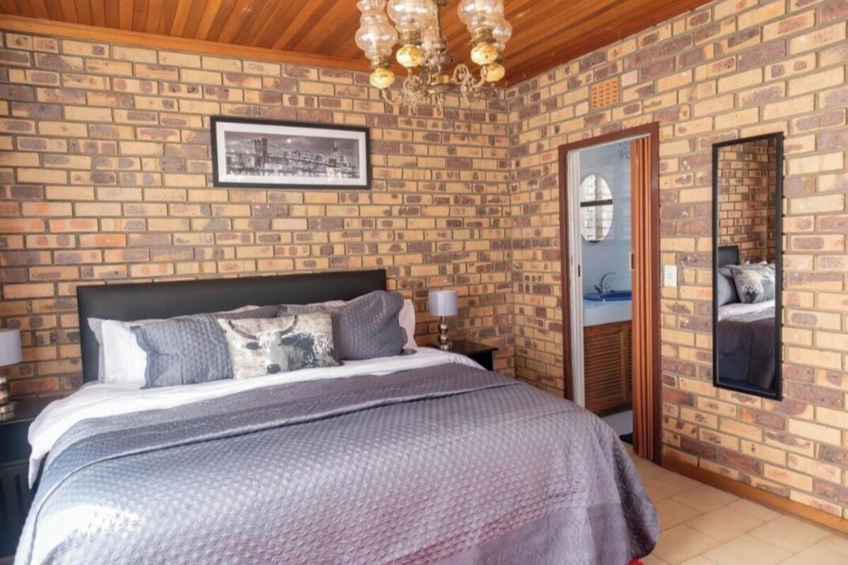 Una camera da letto con parete in mattoni, un letto con copriletto a motivi grigio e bianco, soffitto in legno e un lampadario.