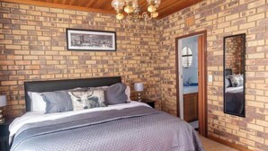Un dormitorio con pared de ladrillo, cama con colcha de diseño gris y blanco, techo de madera y candelabro.
