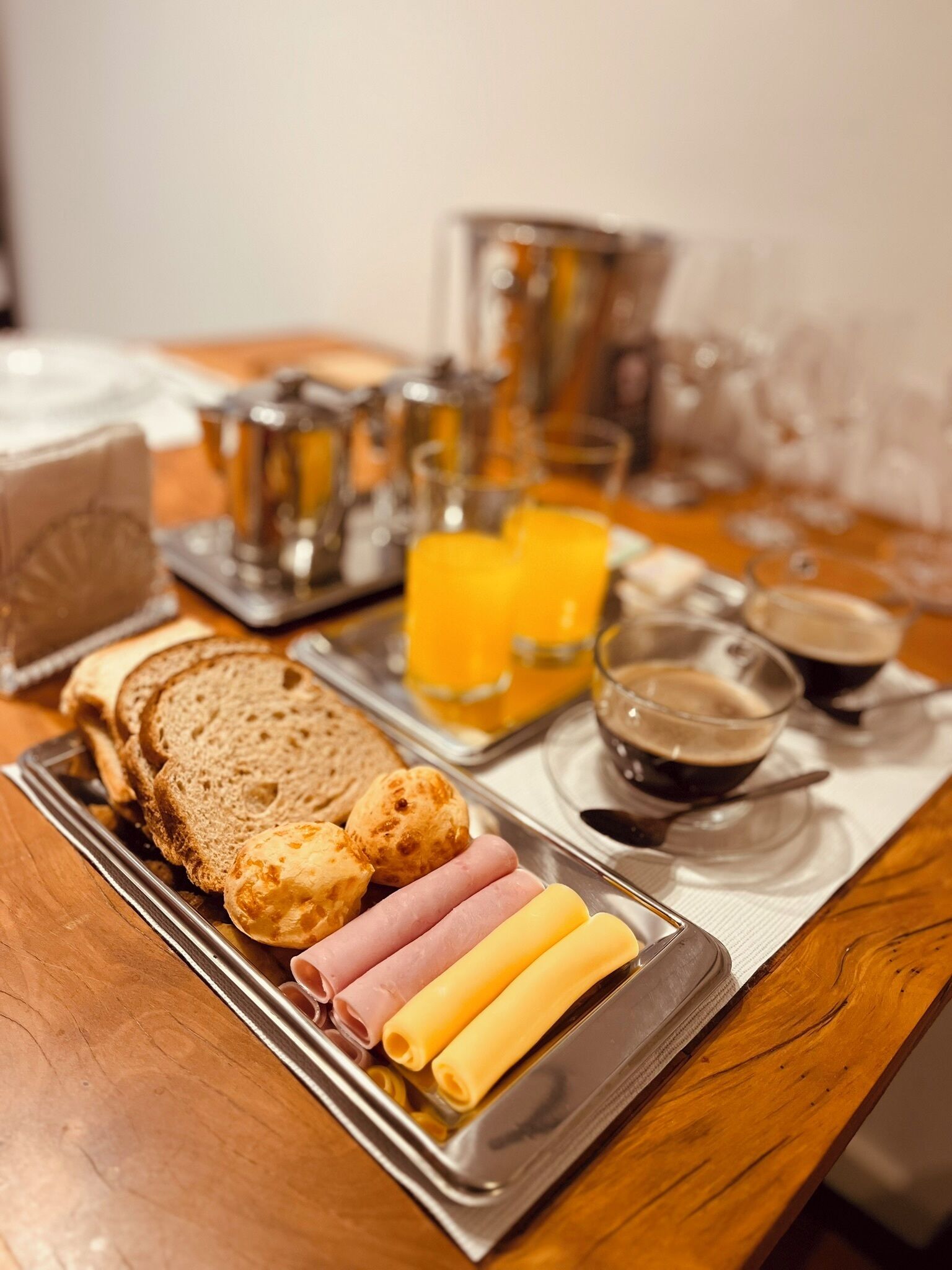 A breakfast tray with bread, sausages, cheese, and orange juice on a wooden table.