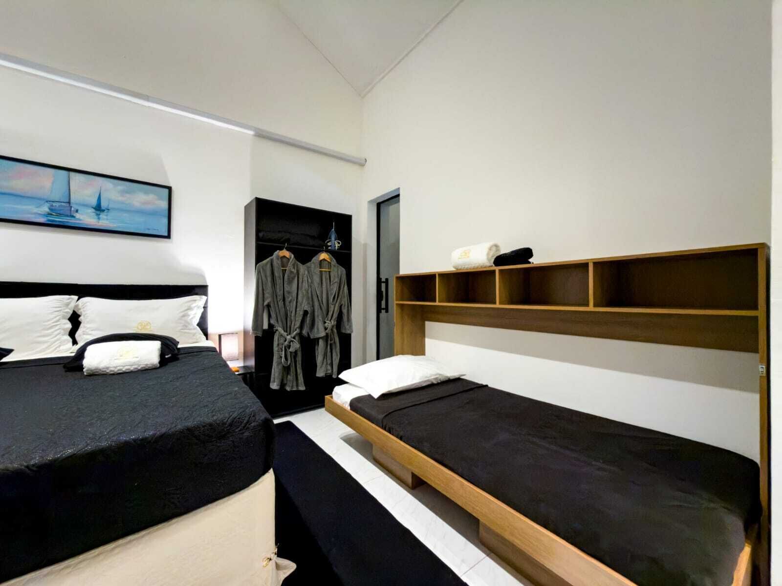 A modern hotel room with two single beds, a wardrobe, and a painting on the wall.
