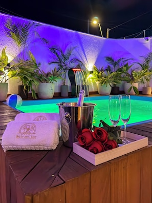 A poolside setting with a metal bucket, two champagne flutes, a tray of red roses, and a towel with a logo.