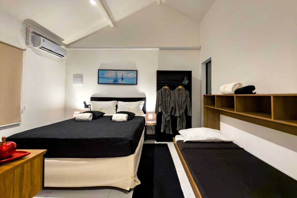 Una camera d'albergo moderna con un letto grande, un letto più piccolo, un armadio e uno scaffale con asciugamani.