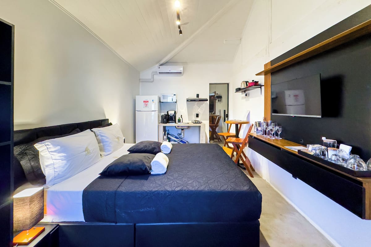 Camera d'albergo compatta con letto, scrivania, sedia, angolo cottura e televisore montato a parete.