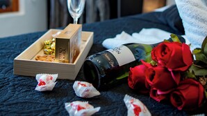A neatly made bed with a bottle of wine, a glass, and a box of chocolates. - Pousada Praia do Carioca (Búzios)