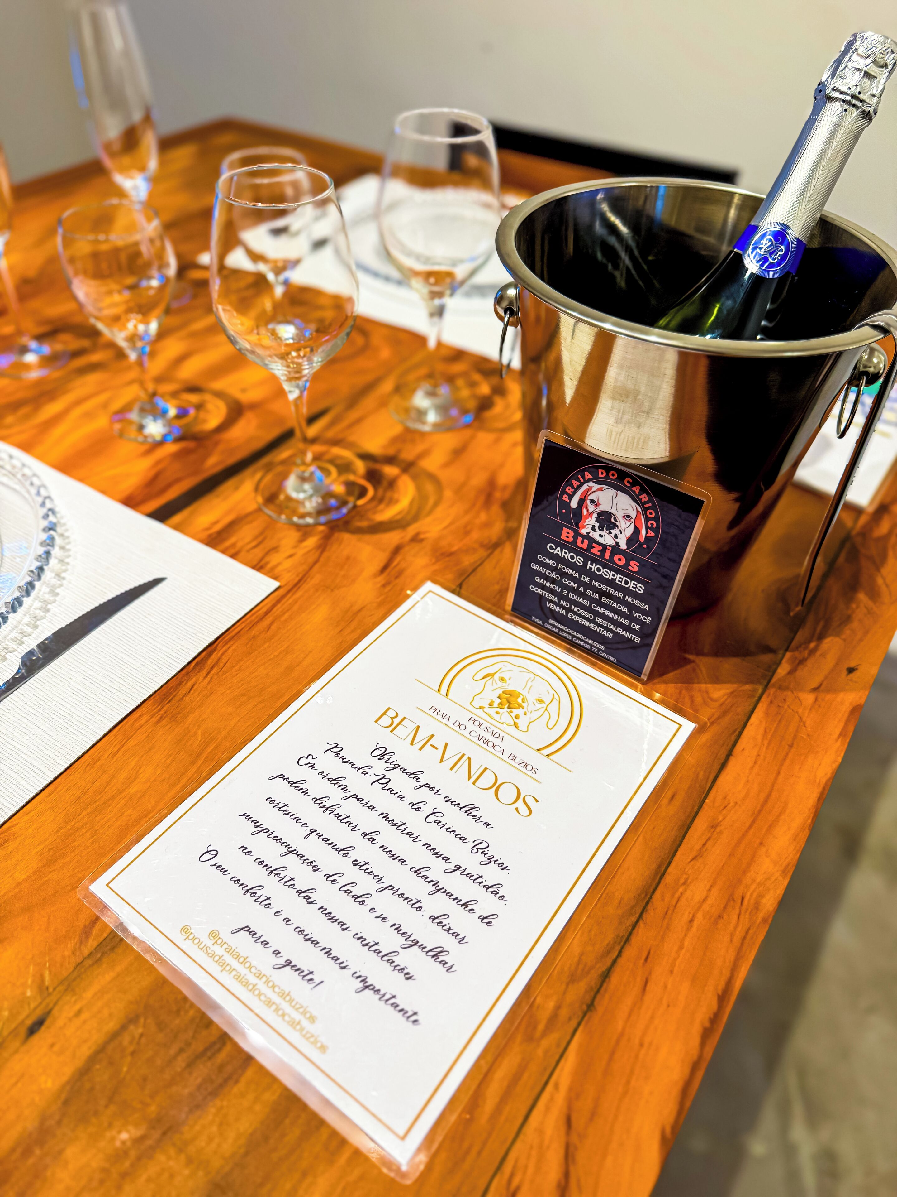 A wooden table with a bottle of champagne in a metal bucket, several empty wine glasses, and a certificate with text.