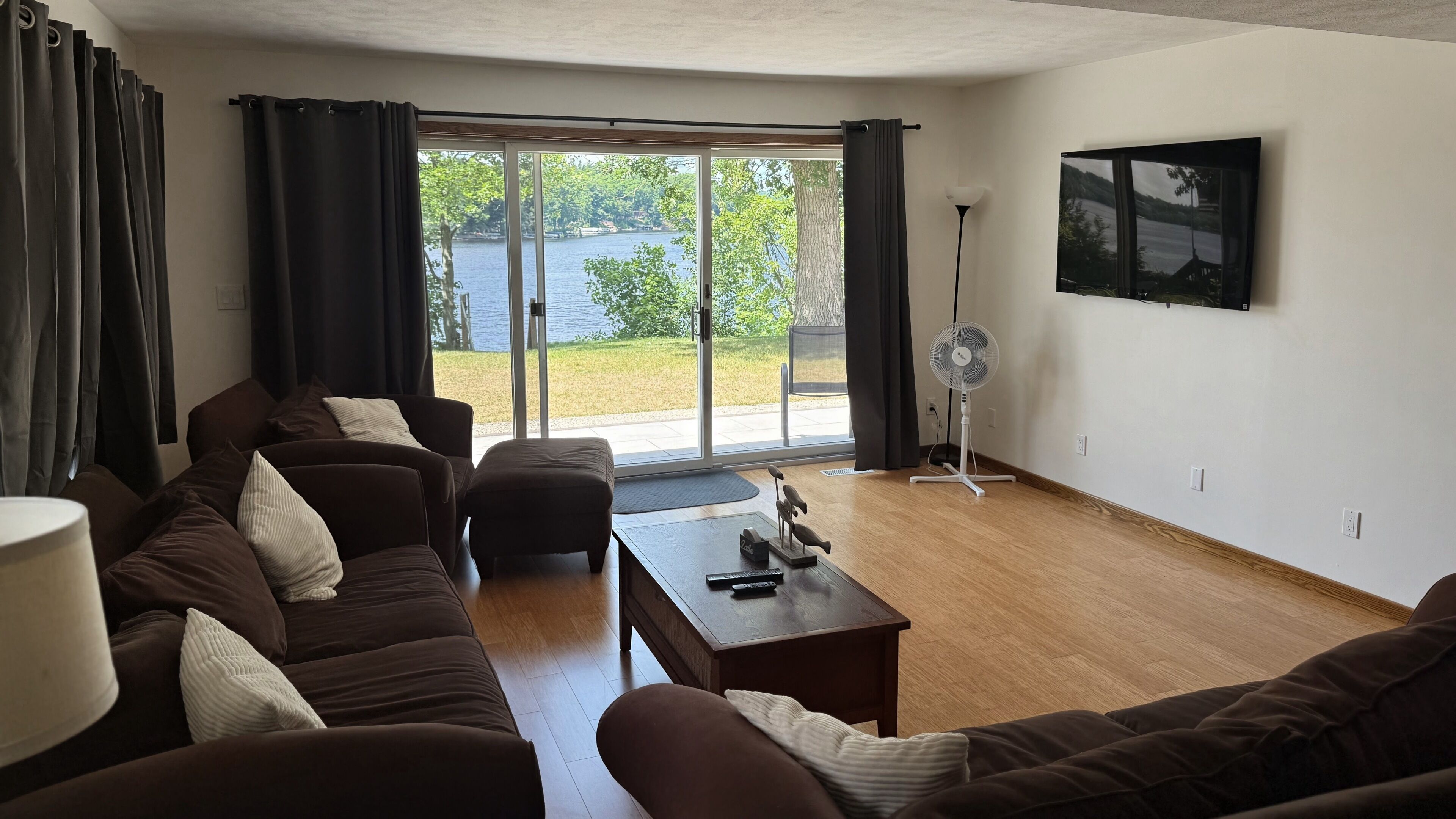Una sala de estar con un sofá marrón, una mesa de centro y vista a un lago a través de amplios ventanales.