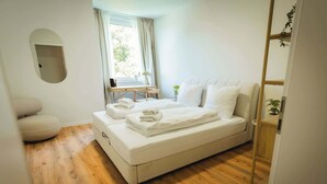 A modern bedroom with a large bed, a bedside table, a chair, and a window with curtains.