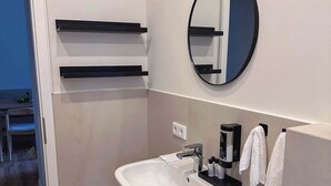 Un baño moderno con un lavamanos blanco, un perchero negro y un espejo redondo.