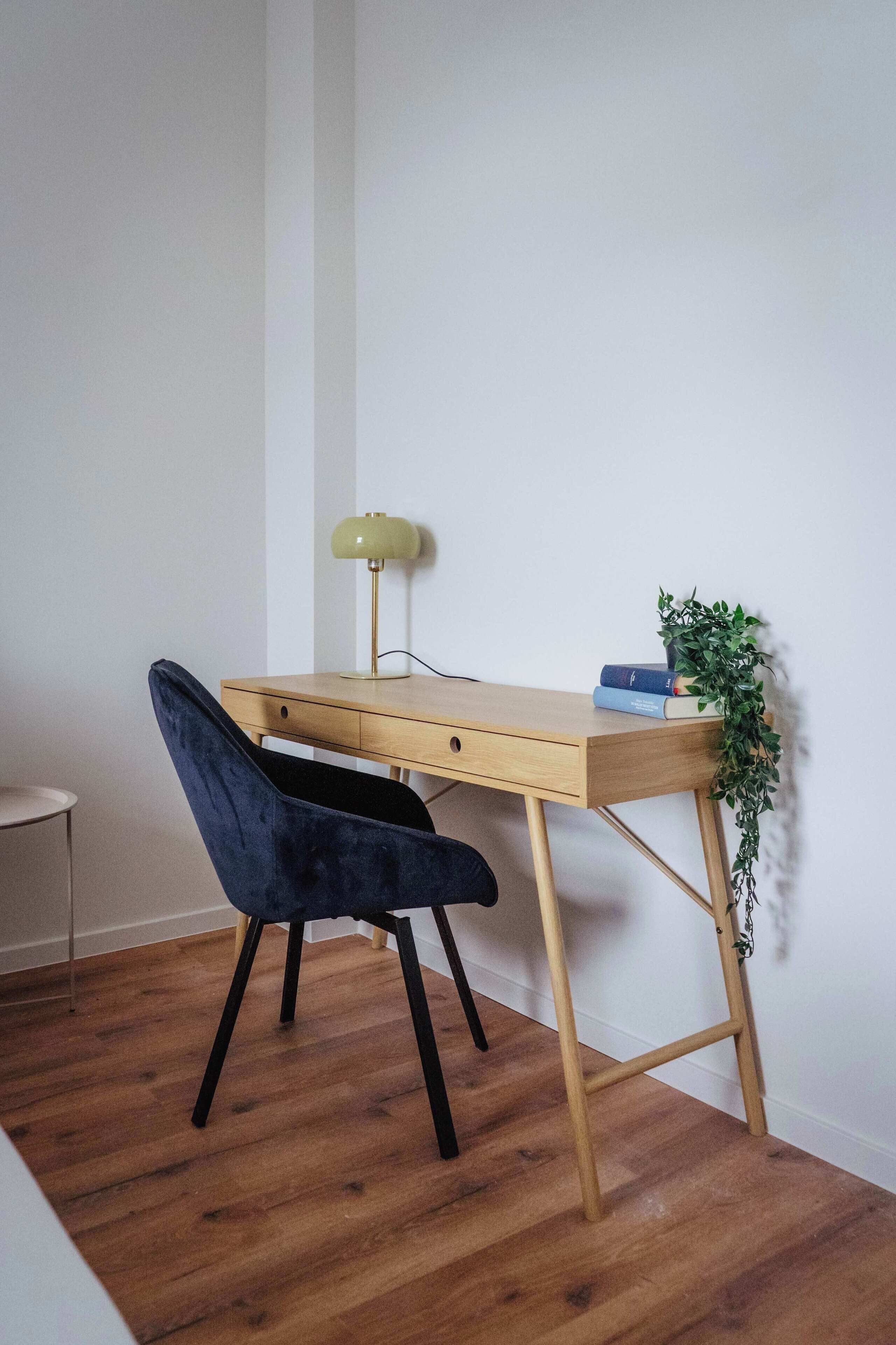 A wooden desk with a green desk lamp, a blue chair, and a small plant.