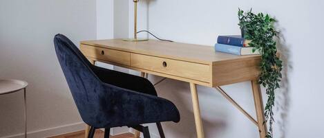 A wooden desk with a green desk lamp, a blue chair, and a small plant.