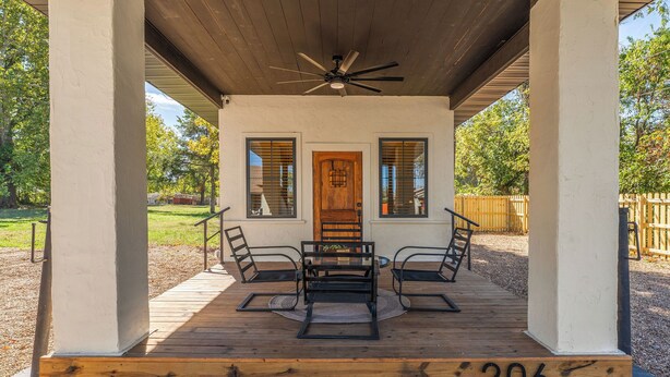 A covered patio with a wooden deck, a ceiling fan, and a door with a window on each side. - Missouri’s 1st Sinclair Service Station (Walnut Grove)
